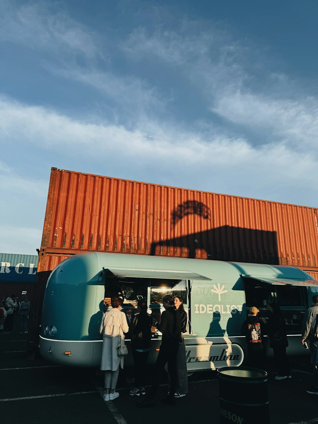 People socialize near a blue food truck with orange containers.