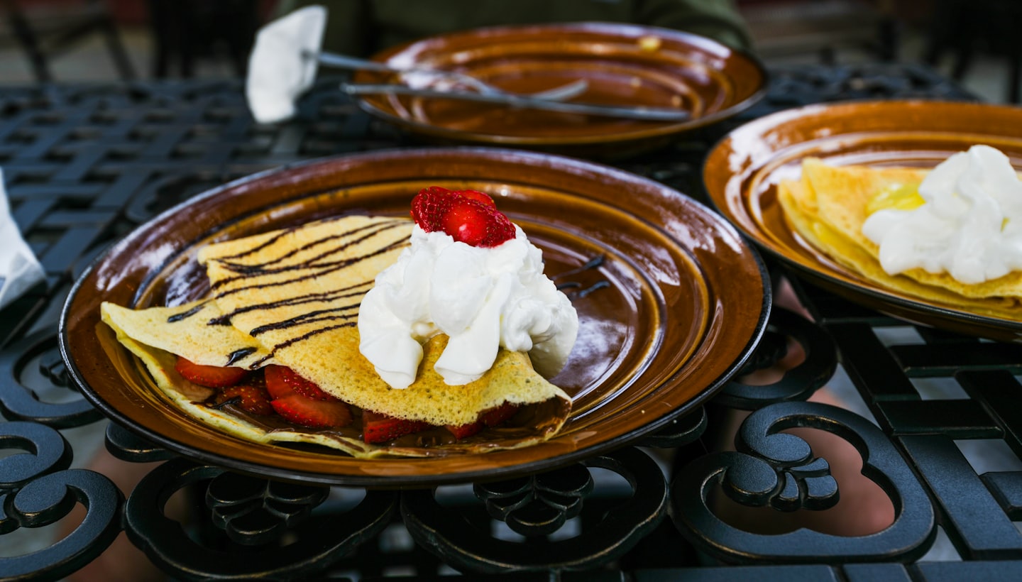 Two dessert crepes with strawberries and whipped cream on an outdoor table.