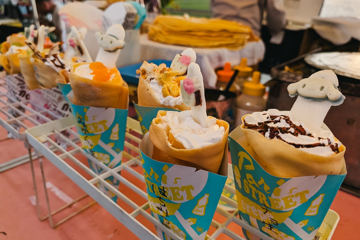 Sweet crepes in paper cones displayed on a metal rack.