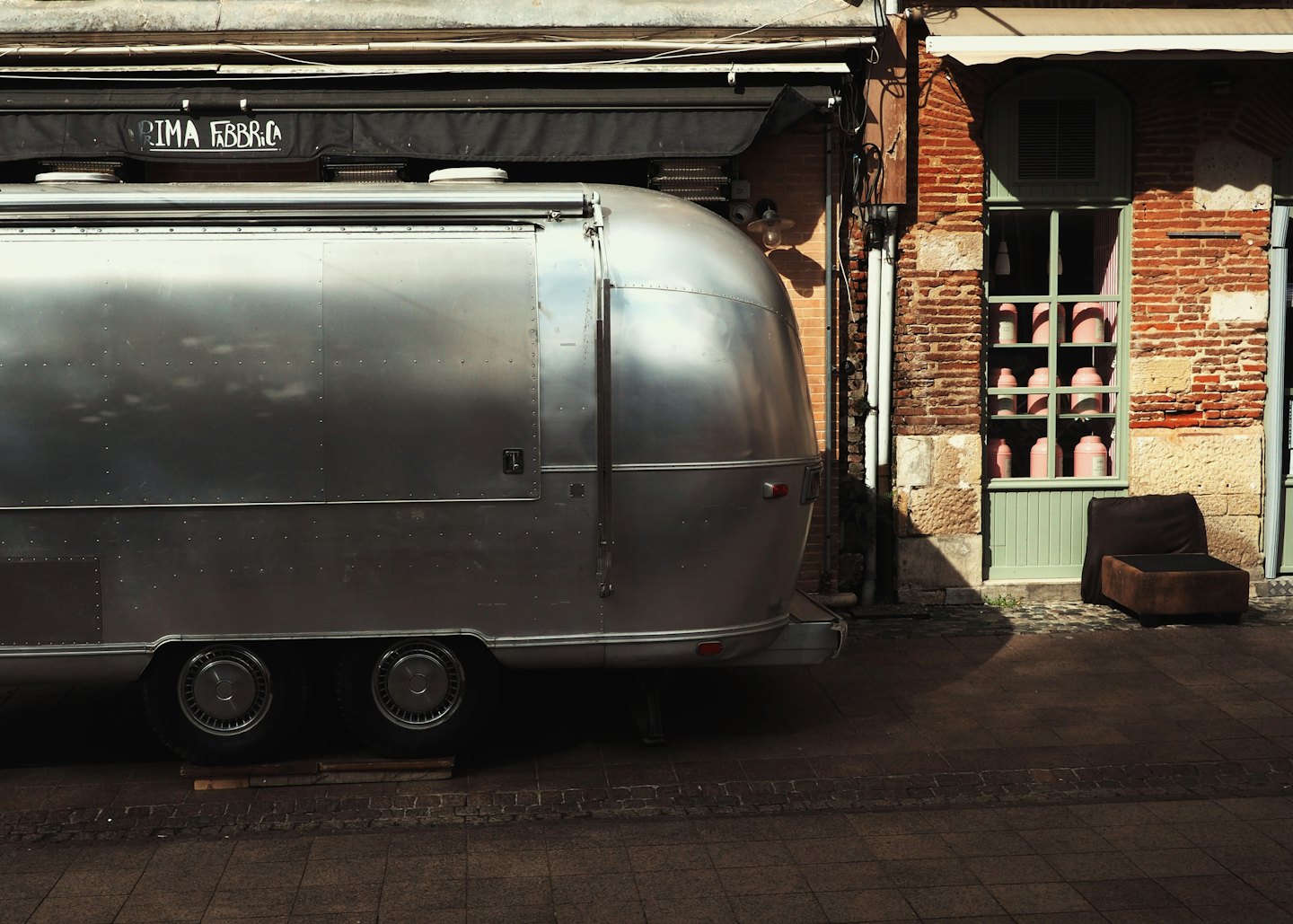 A silver catering trailer parked beside a brick building.