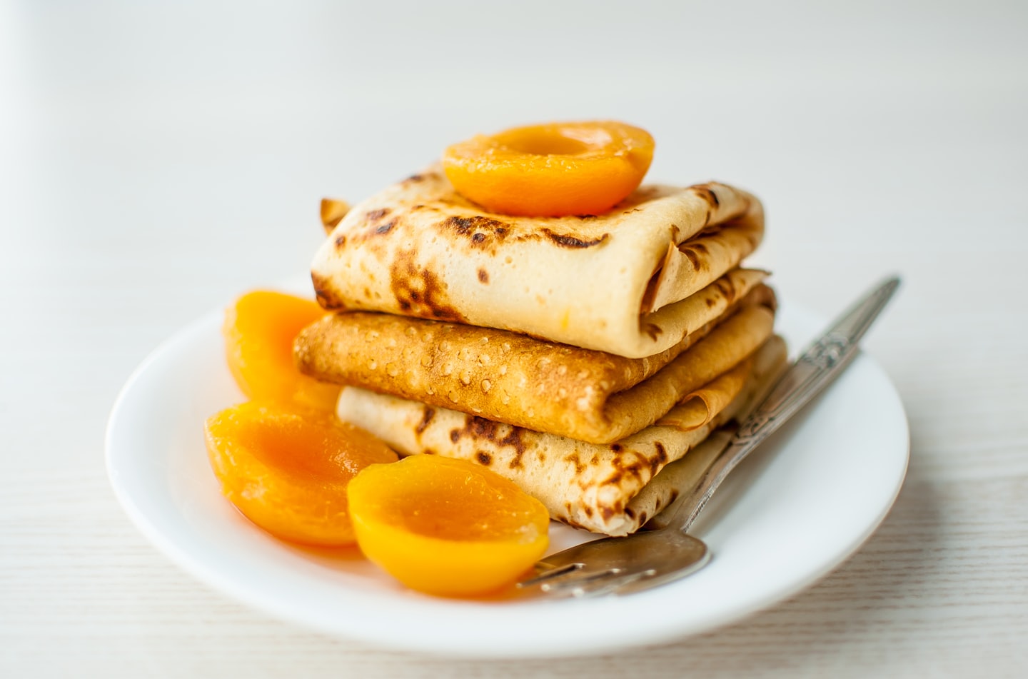 Golden crepes with sliced peaches on a white plate.