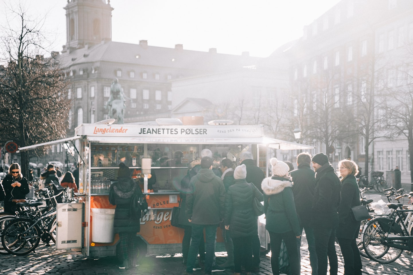People wait in line at a white food truck on a cobblestone street.