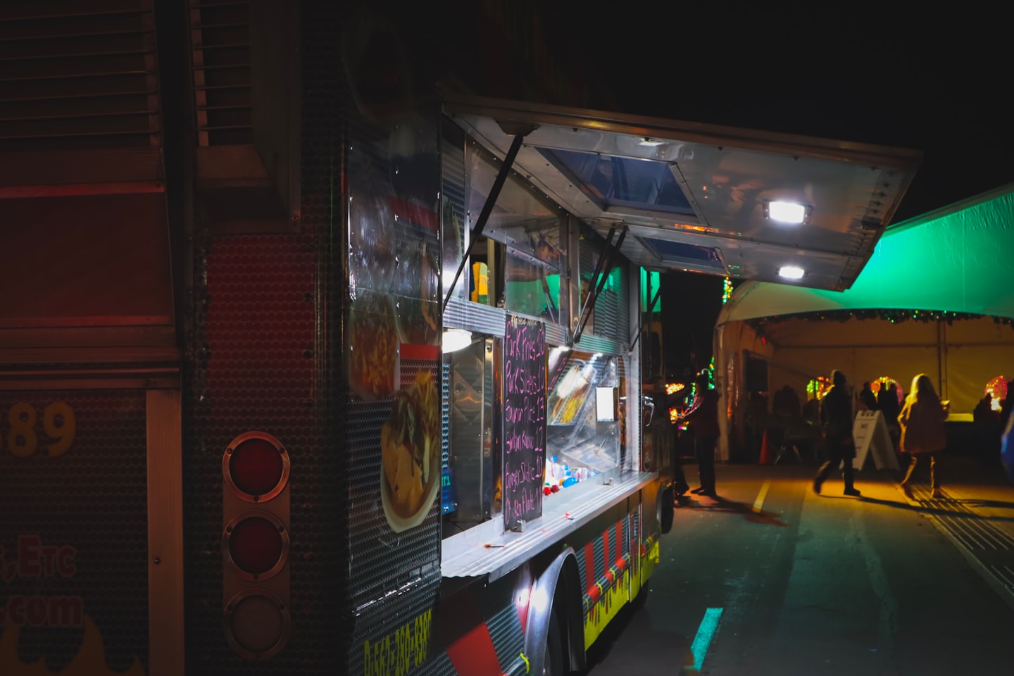 A dark metal food truck serves customers at a night market.