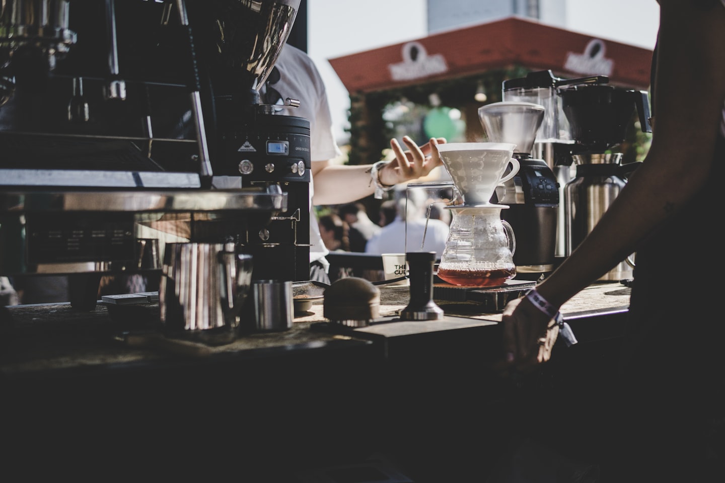 Barista making pour-over coffee at an outdoor coffee bar.