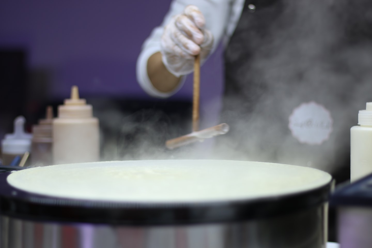 A chef uses a wooden tool to spread crepe batter.