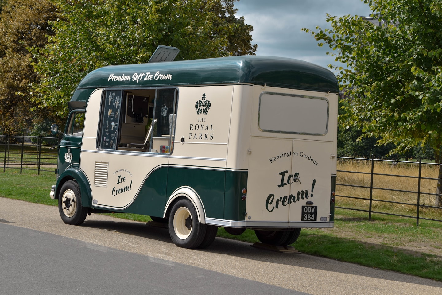 Vintage dark green and cream ice cream truck parked by trees.